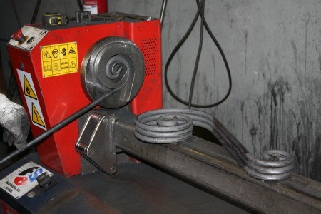 Cómo se fabrica un cabecero de forja, paso a paso en el taller 4 Máquina curvadora del taller doblando una barra de hierro para formar una voluta